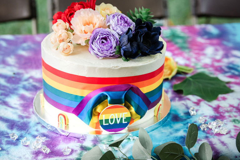 a rainbow wedding cake woth the button saying, "Love".