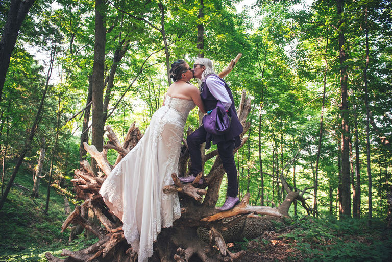 a groom and bride kiss hanging from the root ball of a large tree in Empire.