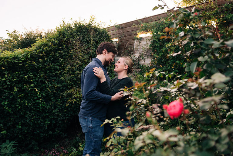 a couple stands in between bushes at the Traverse City Botanical gardens for engagement photos.