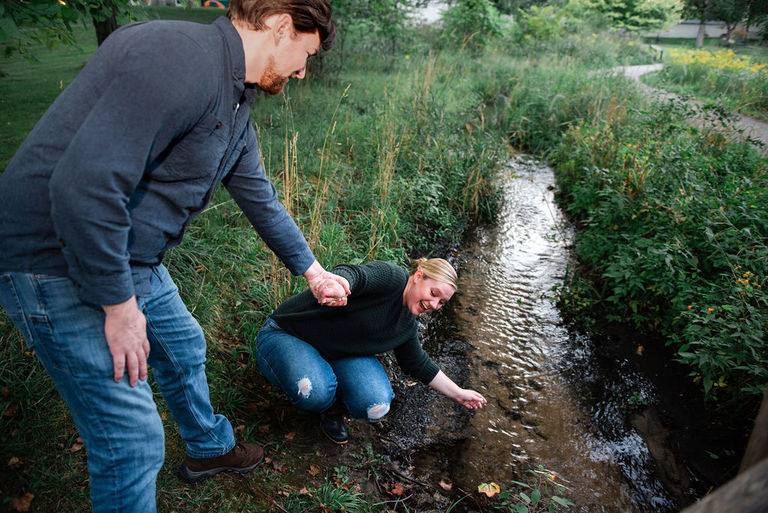 a man holds his fiancé's hand as she try's not to fall into the creek in Traverse City.