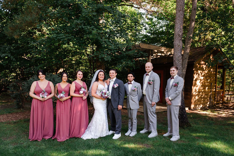 The wedding party stands fir a formal photo in the shade at Blue Bridge Events Center.