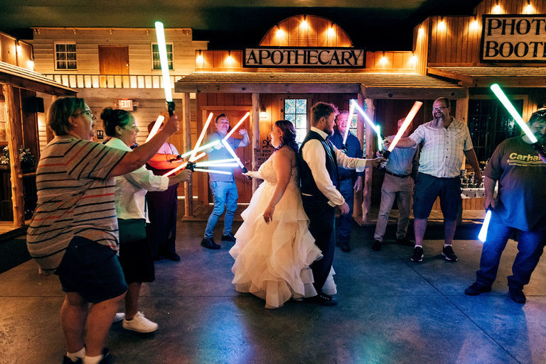 a newly married couple stands back to back armed with lightsabers from the Star Wars movies at Cobblestone Farm.