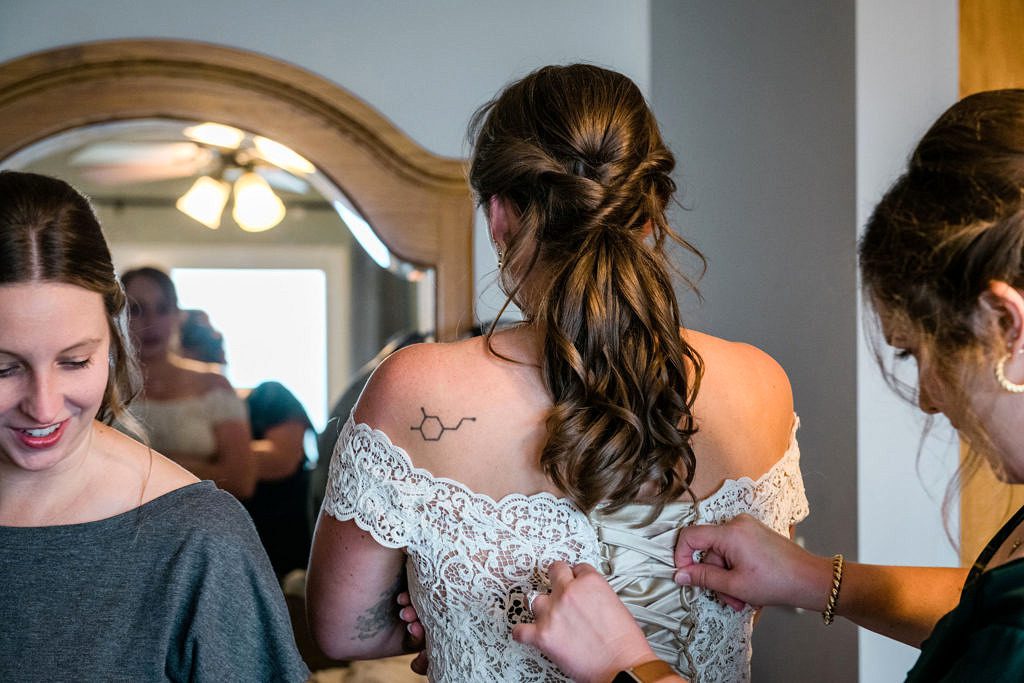 A woman has her wedding corset dress adjusted by her friends.