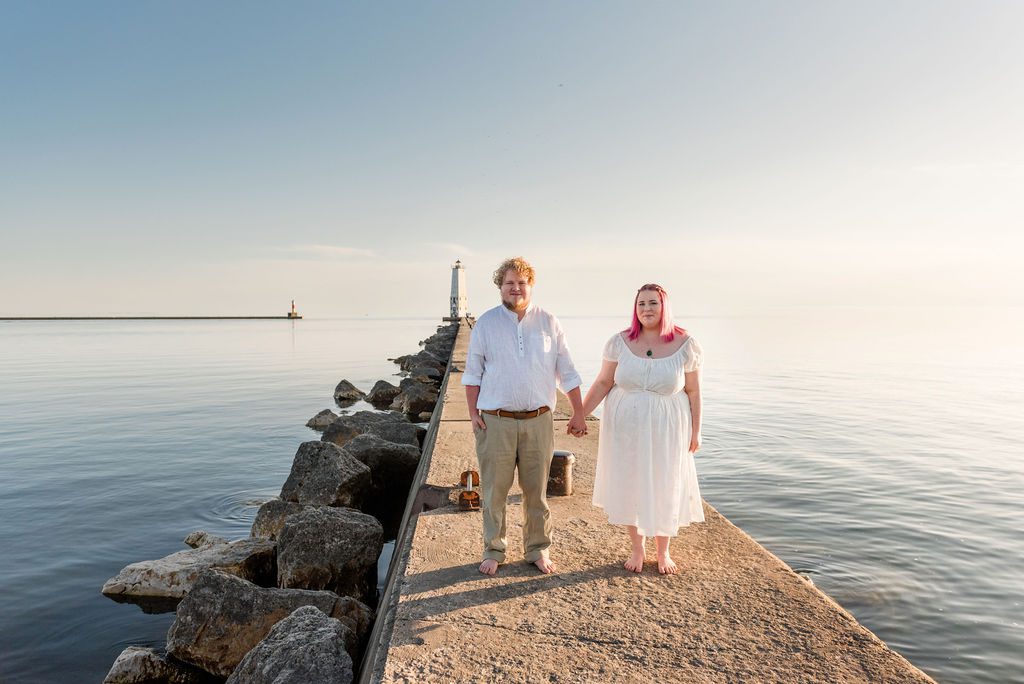 a couple in white at golden hour stands hand in hand at the Frankfort lighthouse.