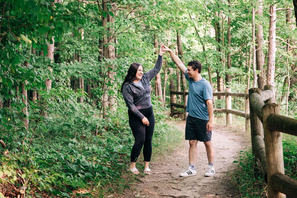 a photo of a man and woman laughing while practicing a first dance twirl on the high rollaway trail for engagement pictures.