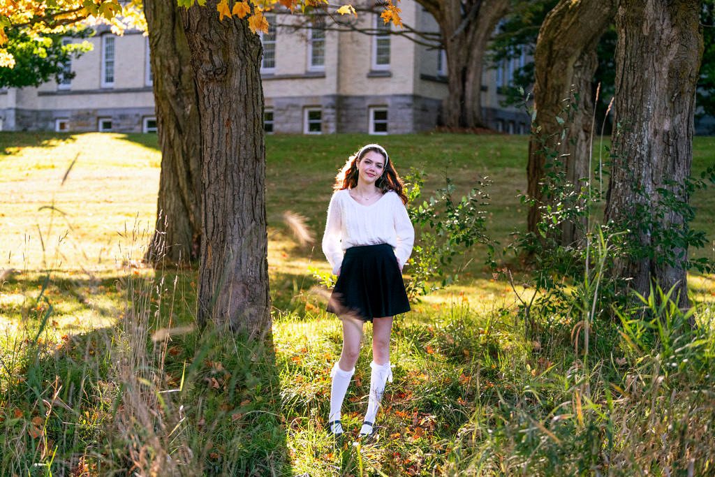 a senior poses in front of the old state hospital in traverse city backlit by the sun.