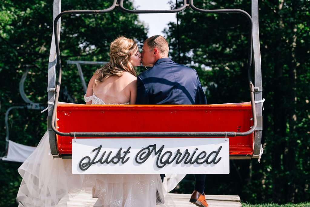 A wedding couple kisses on the ski lift with a just married sign at the homestead resort.