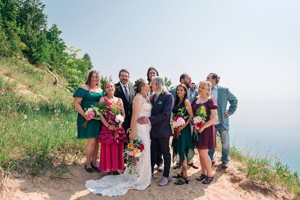 the wedding couple kisses with their party behind them at Sleeping bear dunes.